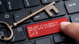 Keyboard with the word Employment Law on one of the keys with a hand pressing it. A led key is in resting on the keyboard.