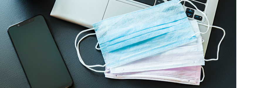 Medical masks on a laptop with a smartphone and antibacterial wipes on a black background.