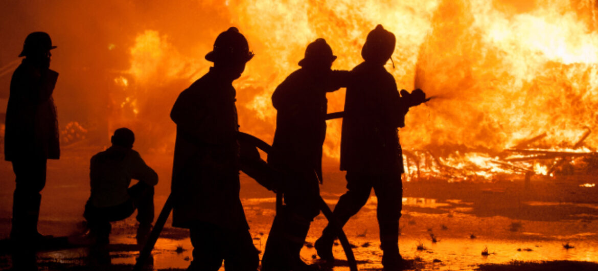 Silhouette of Firemen fighting a raging fire with huge flames of burning timber