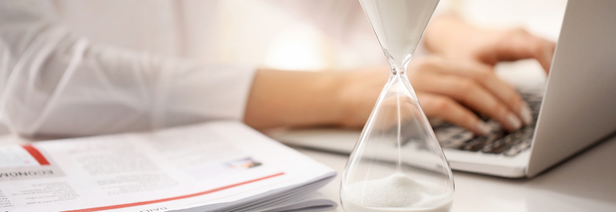 Hourglass and woman working on laptop at table in office