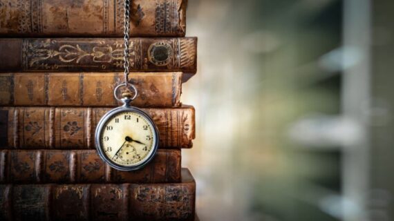 Timepiece dangling over pile of old library books