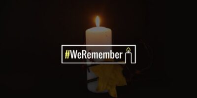 Lit candle against a black background with the hashtag #WeRemember in the foreground