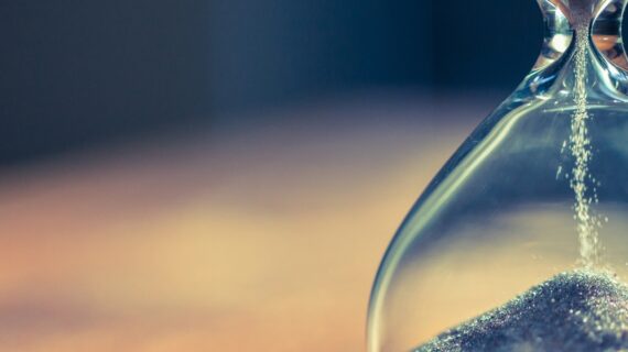 Sand running through the bulbs of an hourglass measuring the passing time in a countdown to a deadline, on a dark background with copy space.