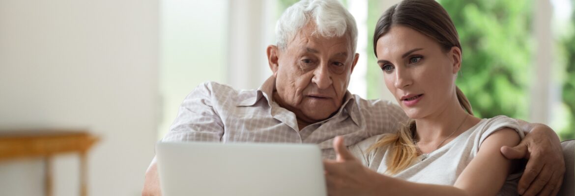 Serious adult daughter helping older father with laptop close up, pointing at screen, explaining, focused young woman teaching mature dad or grandfather to use computer, sitting on couch together