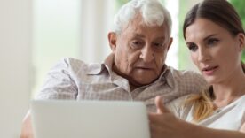 Serious adult daughter helping older father with laptop close up, pointing at screen, explaining, focused young woman teaching mature dad or grandfather to use computer, sitting on couch together