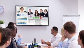 Hybrid meeting - people sitting around a table watching their colleagues join in on a screen