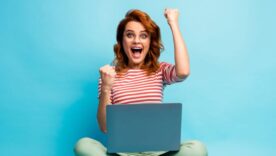 Woman sit with legs crossed work computer with her arms raised in fist pump