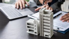 Businessman holding model small building house with property insurance at table in home sales office