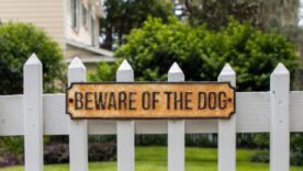 Beware of the dog sign posted on white fence outside a house yard.