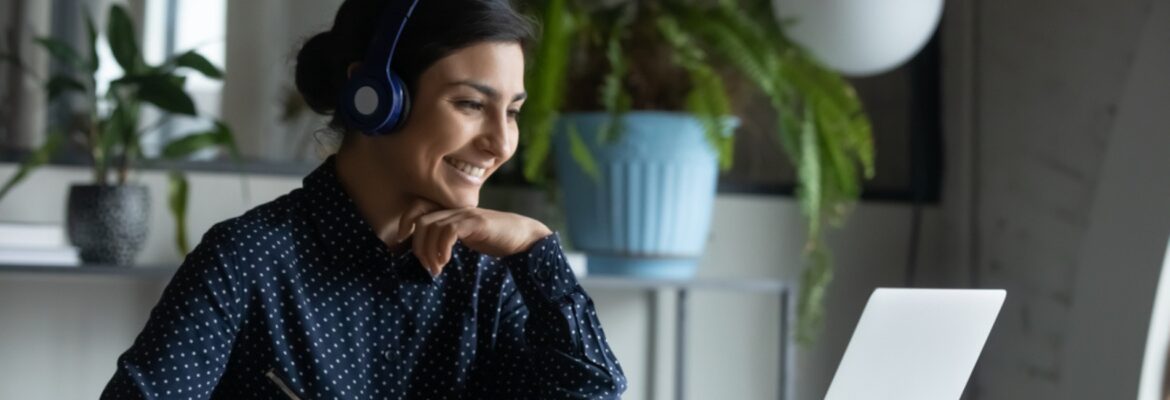 Head shot happy young indian ethnicity female manager wearing wireless headphones, looking at laptop screen, holding pleasant conversation with partners clients online, working remotely at workplace.