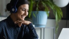 Head shot happy young indian ethnicity female manager wearing wireless headphones, looking at laptop screen, holding pleasant conversation with partners clients online, working remotely at workplace.