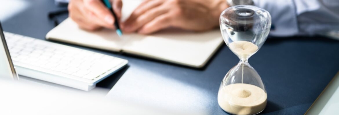 Close-up Of Hourglass In Front Of Businessperson's Hand Calculating Invoice.